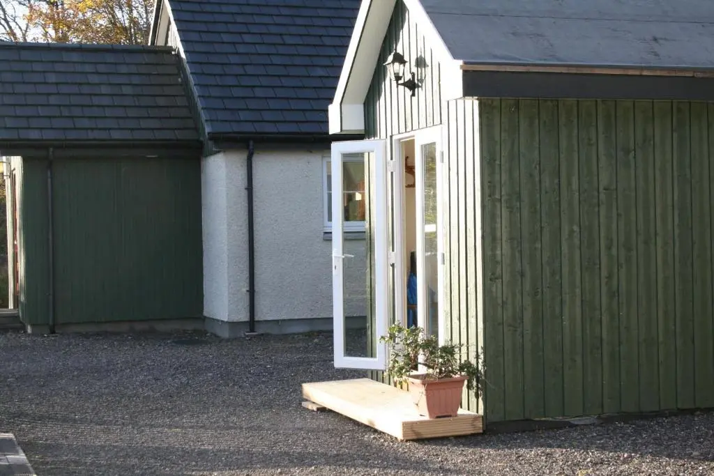 a green building with a door and a potted plant at BCC Loch Ness Hostel in Bearnock