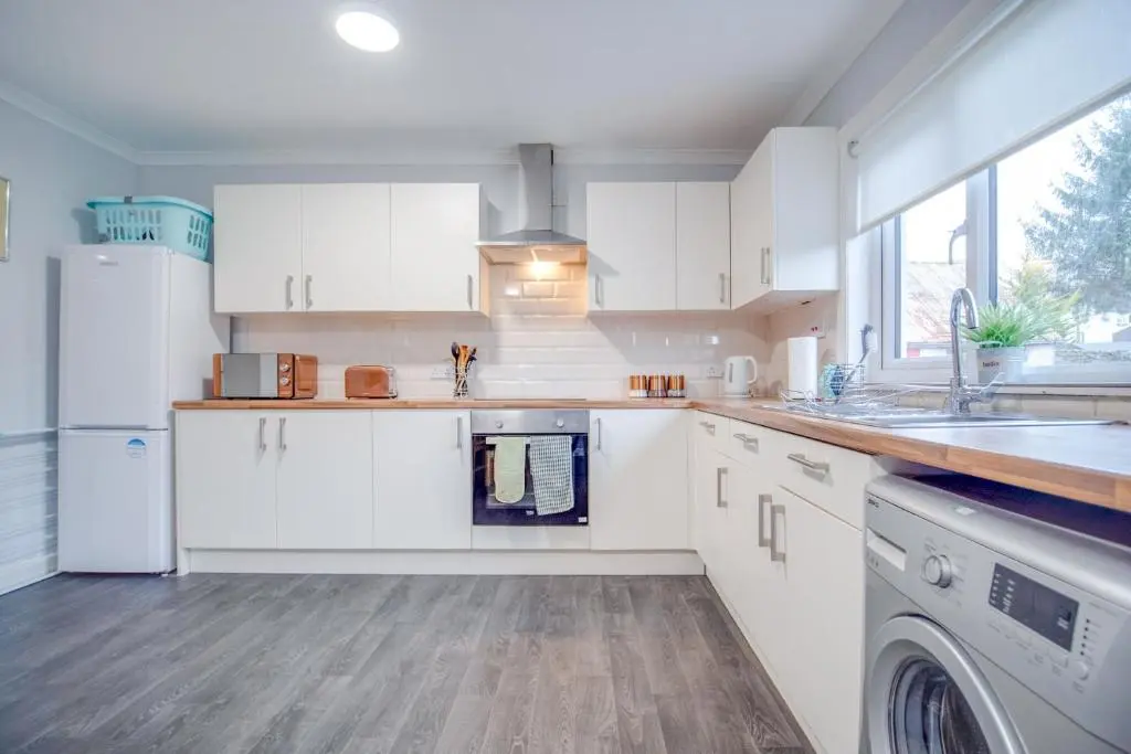 a kitchen with white cabinets and a sink at Novar 4 Bedroom House Alness in Inverness