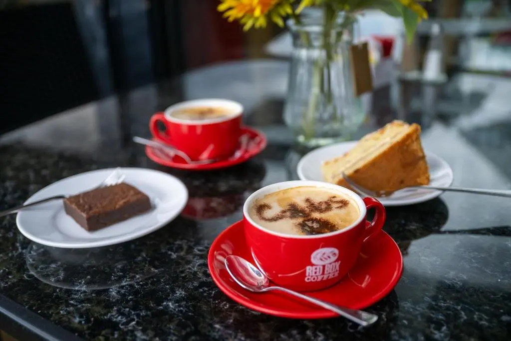 two cups of coffee and a piece of cake on a table at Loch Ness Drumnadrochit Hotel in Drumnadrochit