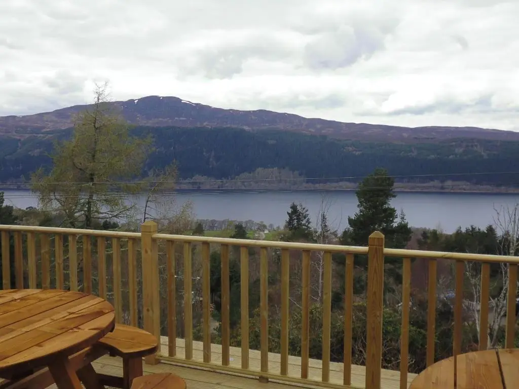 a wooden deck with a table and a view of a lake at Foyers House in Foyers