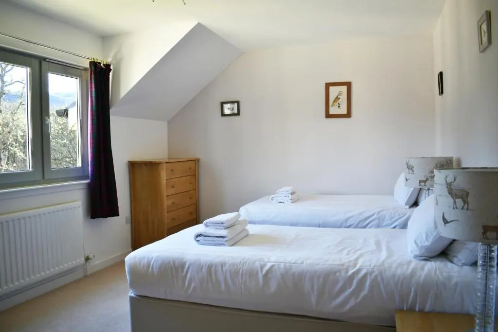 a bedroom with two beds and a window at Abbey Holidays Loch Ness Luxury Self Catering 2 Bedroom Cottages in Fort Augustus