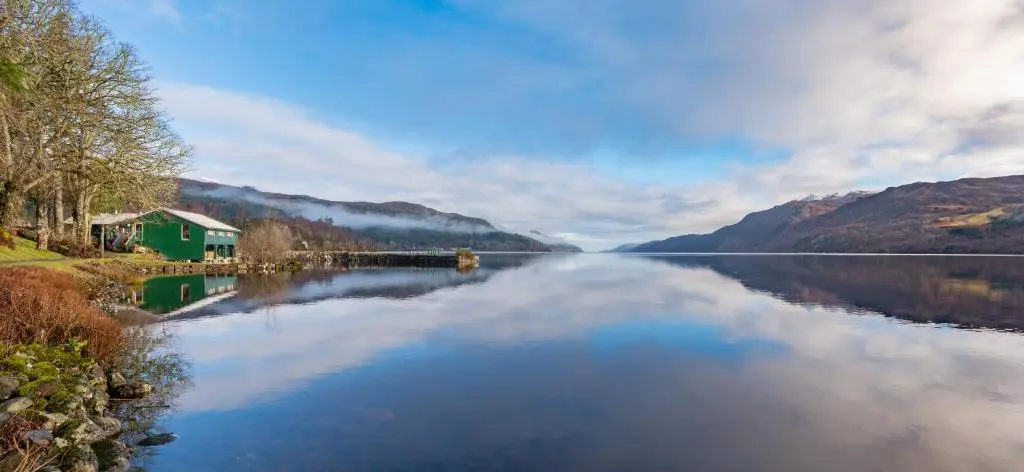 a view of a lake with a house and mountains at The Caledonian 3 Bedroom Self Catering Apartment in historic Abbey in Fort Augustus