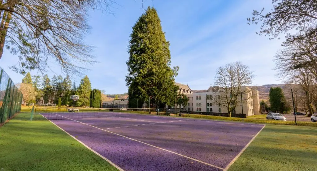 an empty tennis court in front of a building at The Caledonian 3 Bedroom Self Catering Apartment in historic Abbey in Fort Augustus
