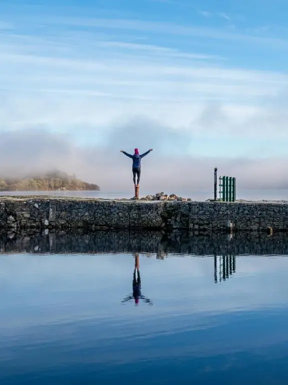 a person standing on a pier with their arms out over the water at The Caledonian 3 Bedroom Self Catering Apartment in historic Abbey in Fort Augustus