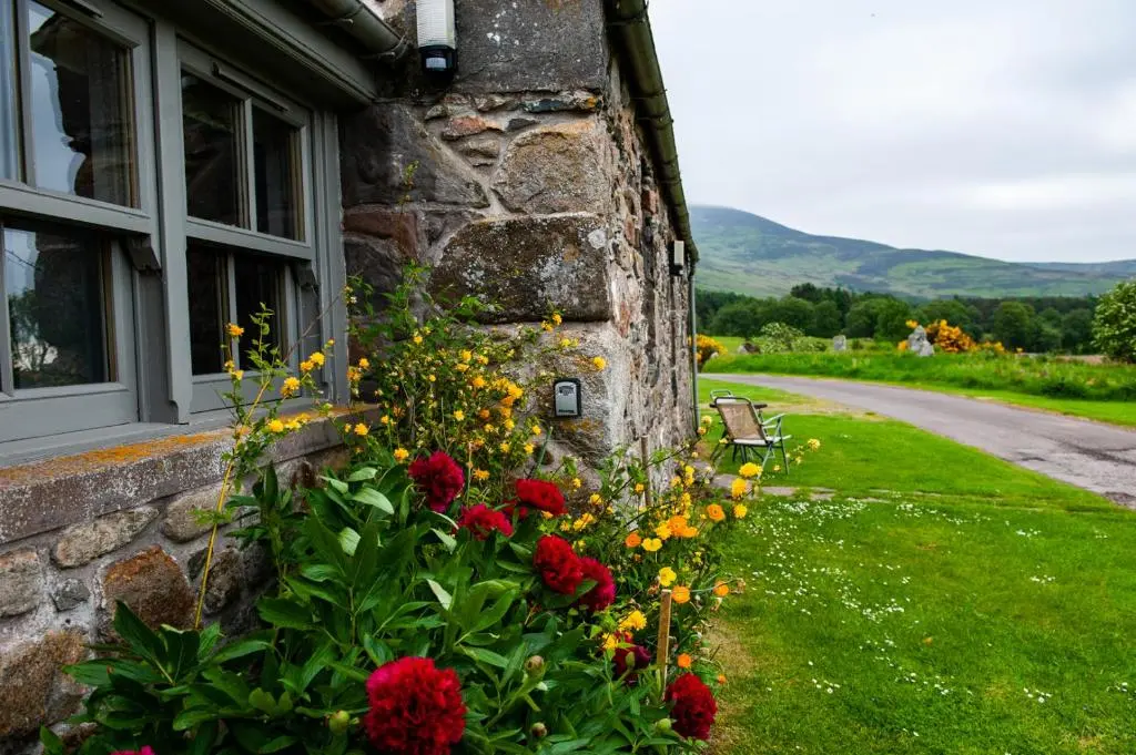 a stone house with a flower garden next to a window at Colmeallie Bothy - Seasgair Lodges in Brechin