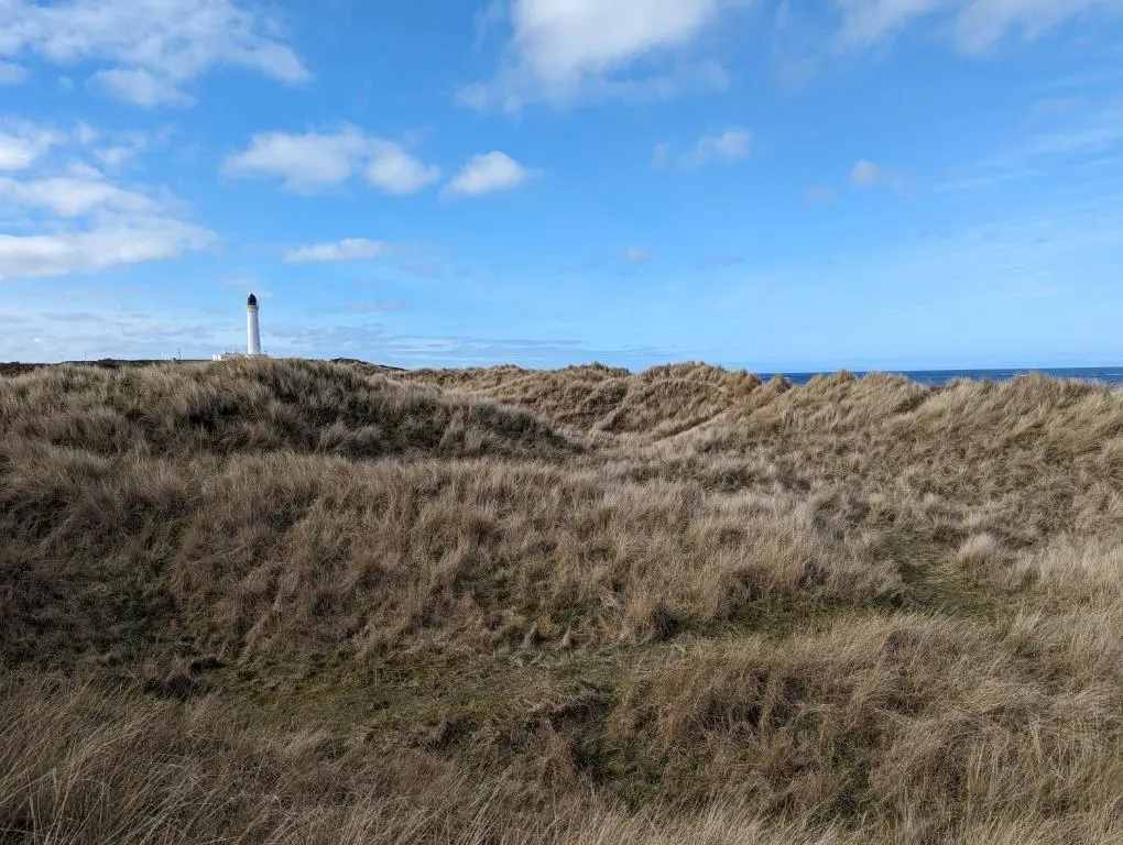 a grassy hill with a lighthouse on top of it at D11 - the Dunes at Silver Sands in Lossiemouth