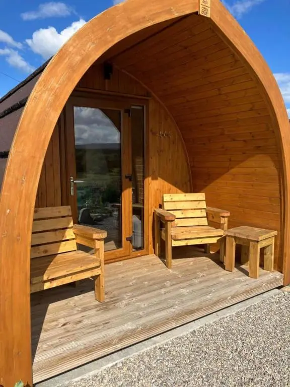a wooden cabin with two benches and a patio at Migdale Pods Luxury Glamping in Bonar Bridge