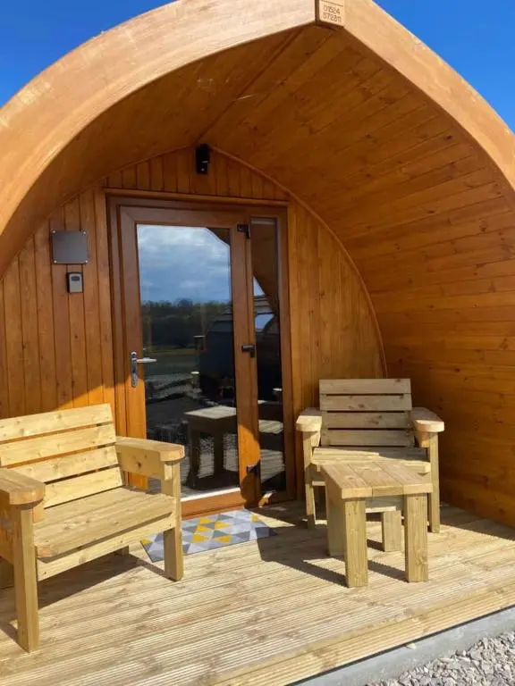 a wooden cabin with two benches and a patio at Migdale Pods Luxury Glamping in Bonar Bridge