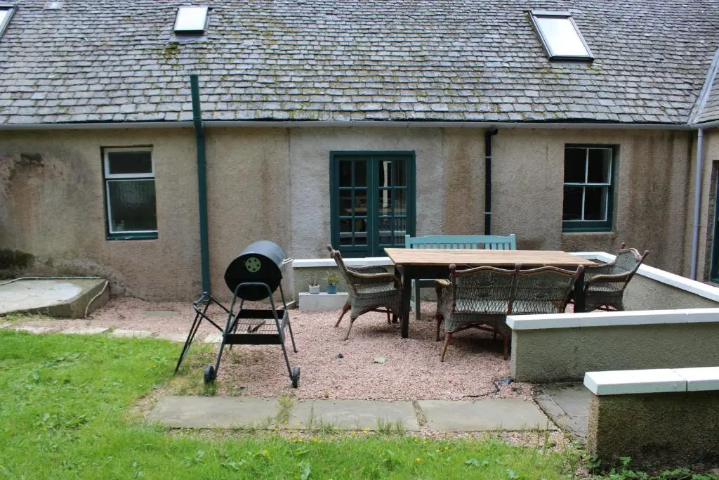 a grill and a table and chairs in front of a house at Spacious Cottage in the Grounds of a Scottish Castle in Insch