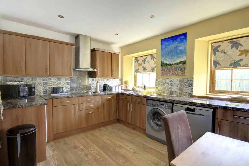 a kitchen with wooden cabinets and a washer and dryer at The Apartment at Allt-Sagart in Golspie