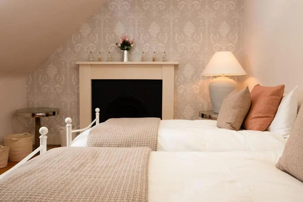 two white beds in a bedroom with a fireplace at The Dell of Rothiemurchus - Seasgair Lodges in Aviemore