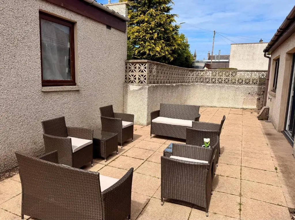 a patio with chairs and tables and a fence at Modern Coastal Retreat, 5-Bedroom, 4-Bathroom Home, with Parking in Portsoy in Portsoy