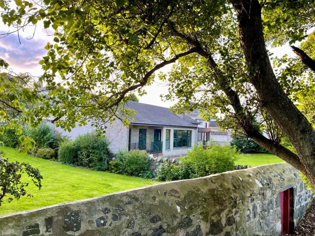a house with a stone wall in front of a yard at Modern Coastal Retreat, 5-Bedroom, 4-Bathroom Home, with Parking in Portsoy in Portsoy