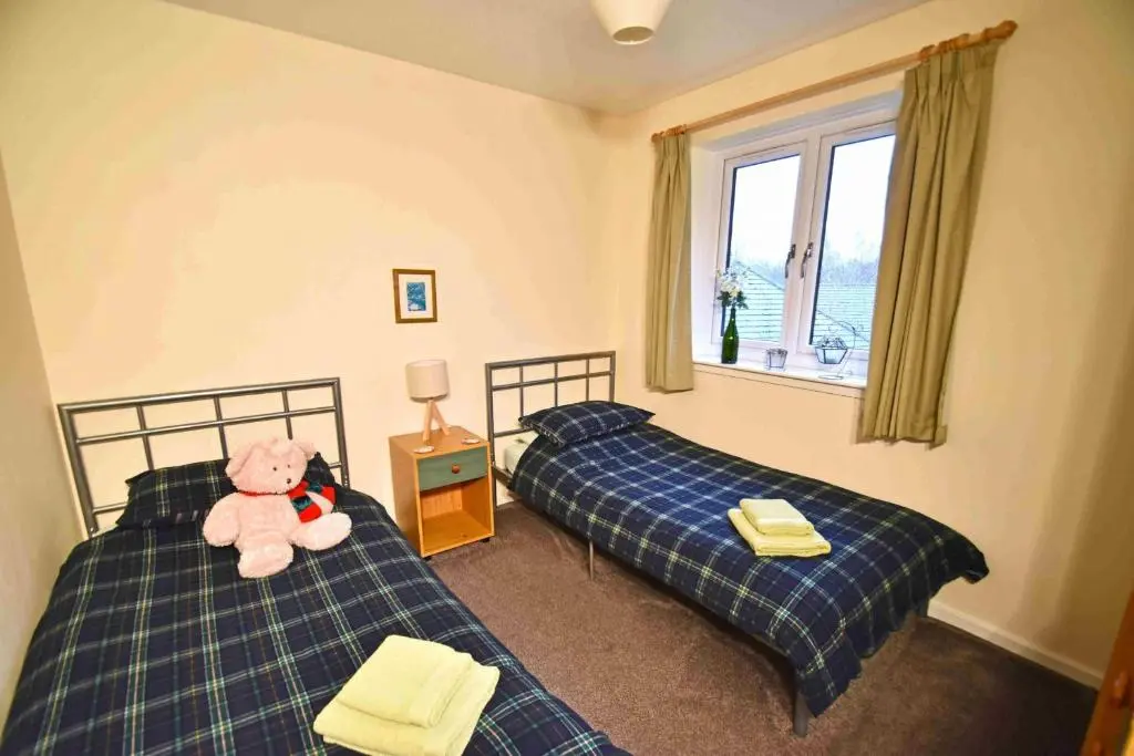 a teddy bear sitting on two beds in a bedroom at Birch View in Aviemore