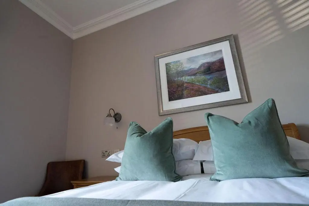 a bedroom with a bed with blue pillows and a painting at The Forbes Arms Hotel in Alford