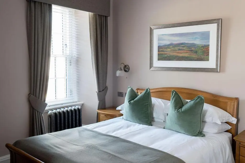 a bedroom with a bed with green pillows at The Forbes Arms Hotel in Alford