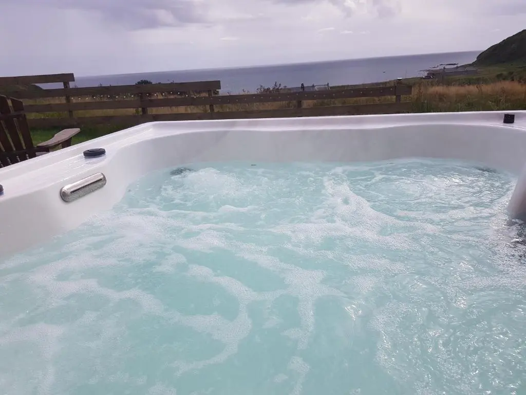 a jacuzzi tub filled with water with the ocean in the background at Bruadarach 'Visionary, Dreamer' in Dunbeath