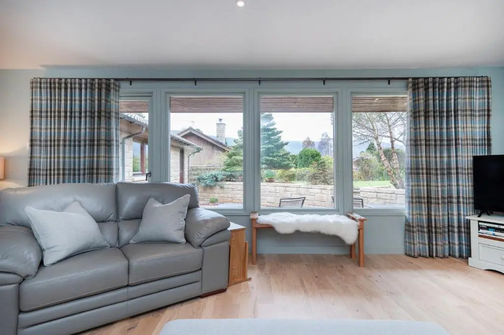 a living room with a couch and large windows at Greenwood - Stunning Scandinavian Style Home in the heart of Ballater Royal Deeside in Ballater