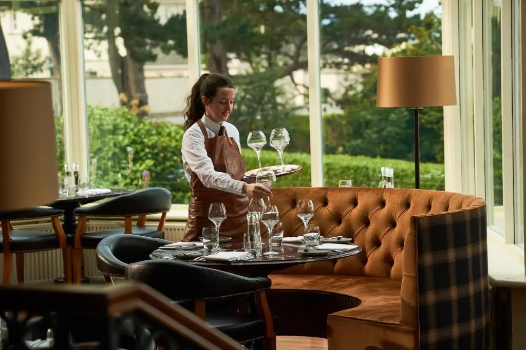 a woman standing in a restaurant holding a tray of wine glasses at Golf View Hotel & Spa in Nairn