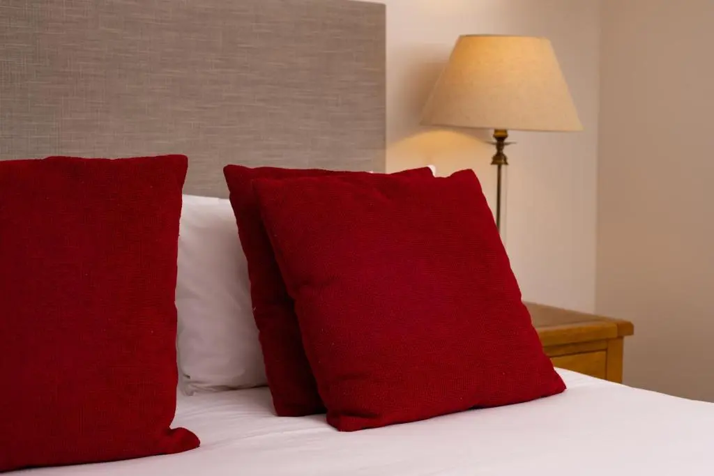 a bed with two red pillows and a lamp at Courtyard Cottage 3, Riverside Cottage in Fort Augustus