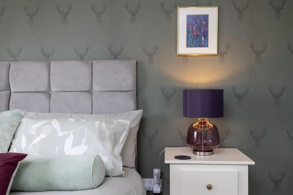 a bed with a purple lamp on a night stand at Orcadia Sutherland Road Dornoch IV25 3SX in Dornoch