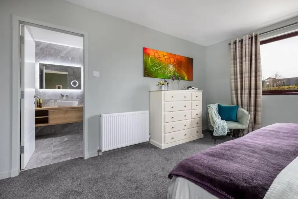 a bedroom with a bed and a sink and a mirror at Orcadia Sutherland Road Dornoch IV25 3SX in Dornoch