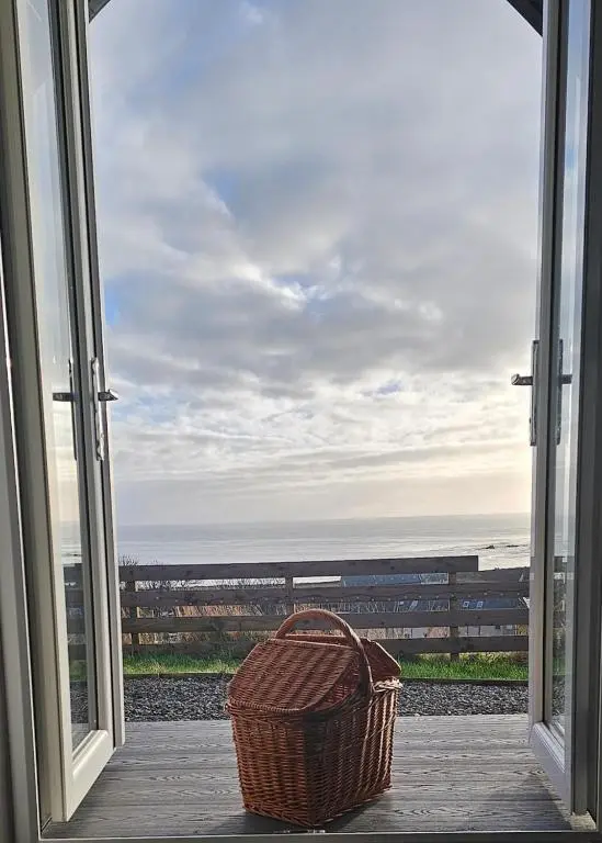 a wicker basket sitting on a porch looking out at the ocean at Camhanaich 'Half light of dawn' in Dunbeath