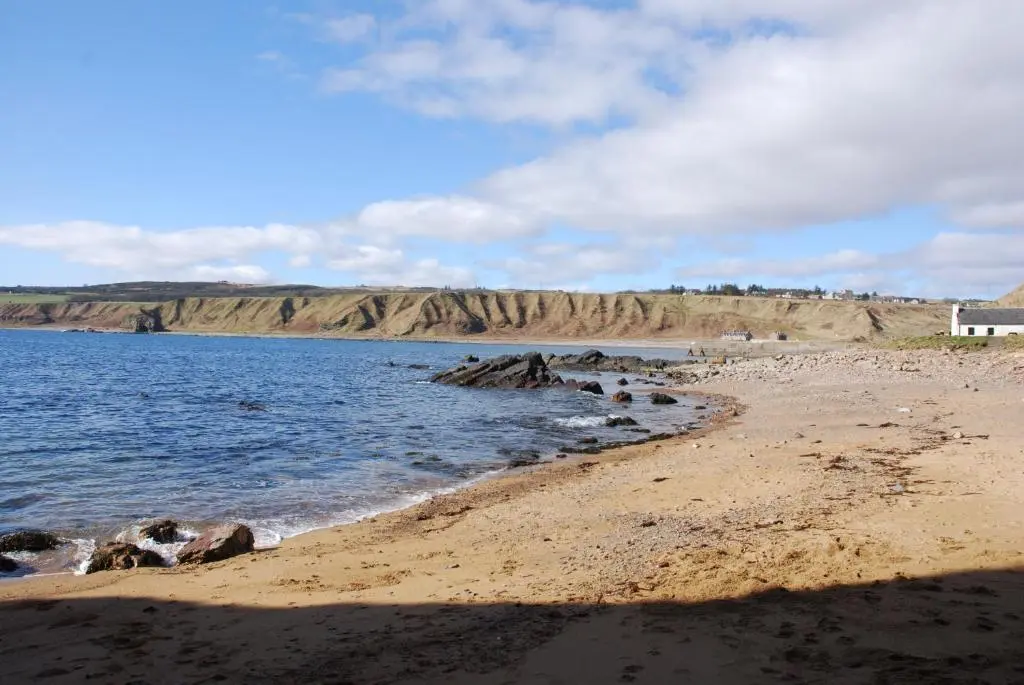 a beach with a house on the shore of a body of water at Camhanaich 'Half light of dawn' in Dunbeath