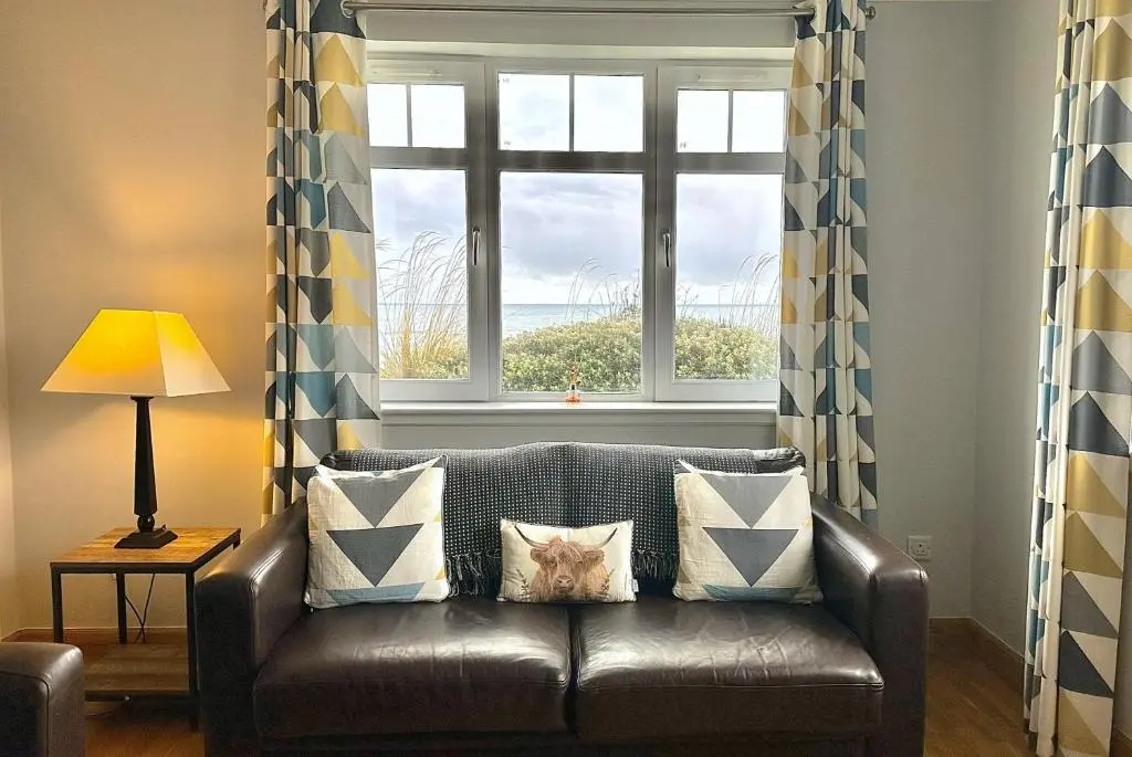 a leather couch in a living room with a window at No2 The Links Apartment, Brora in Brora