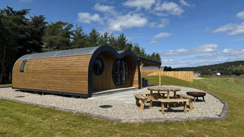 a wooden cabin with a picnic table and a grill at Juniper Lodges in Inverness