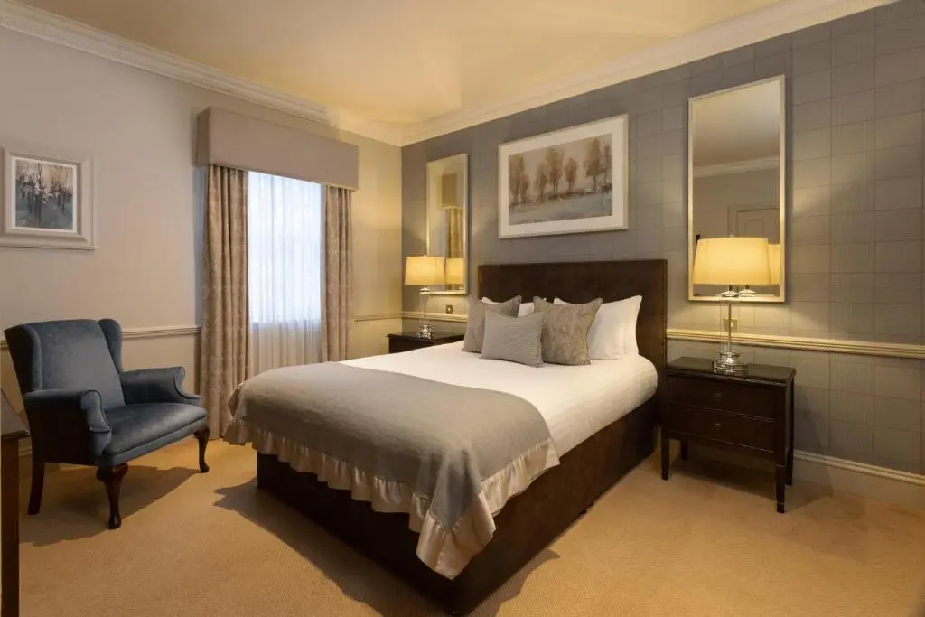 a bedroom with a bed and a chair and a mirror at Thainstone House in Inverurie