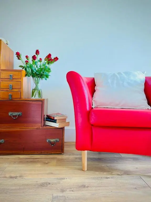 a red chair next to a dresser with a vase of flowers at Cosy Country House in Deeside in Finzean