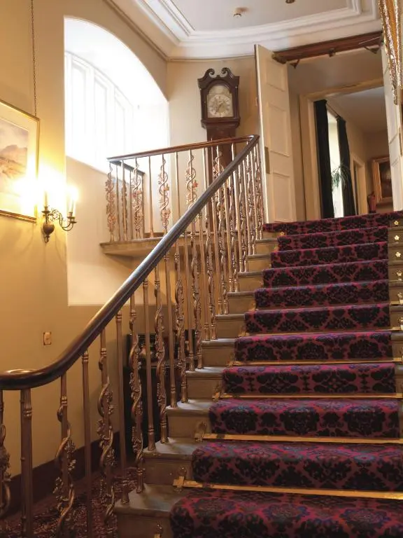 a staircase in a building with a clock on the wall at Macdonald Pittodrie House in Chapel of Garioch