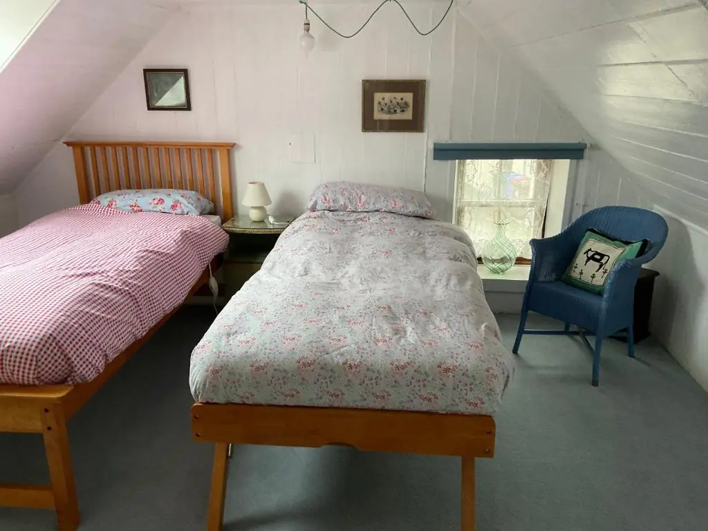 a bedroom with two beds and a chair in a attic at A cosy seaside cottage in Cullen