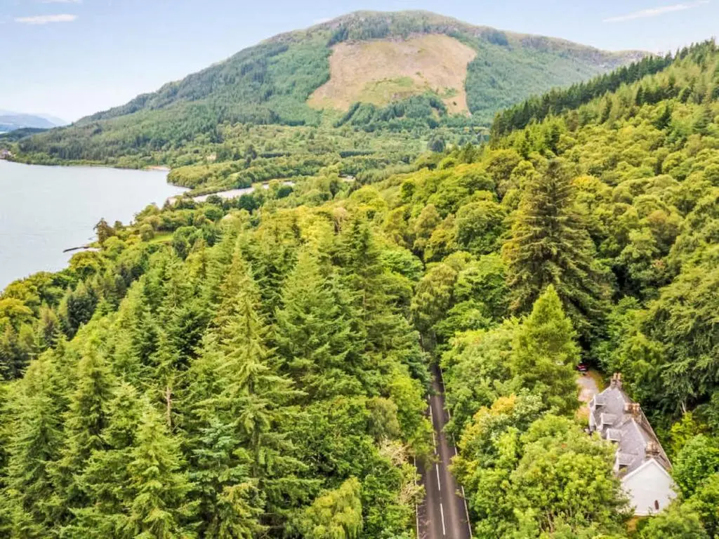 a road through a forest next to a river and a mountain at Holiday Home Dancot by Interhome in Invermoriston