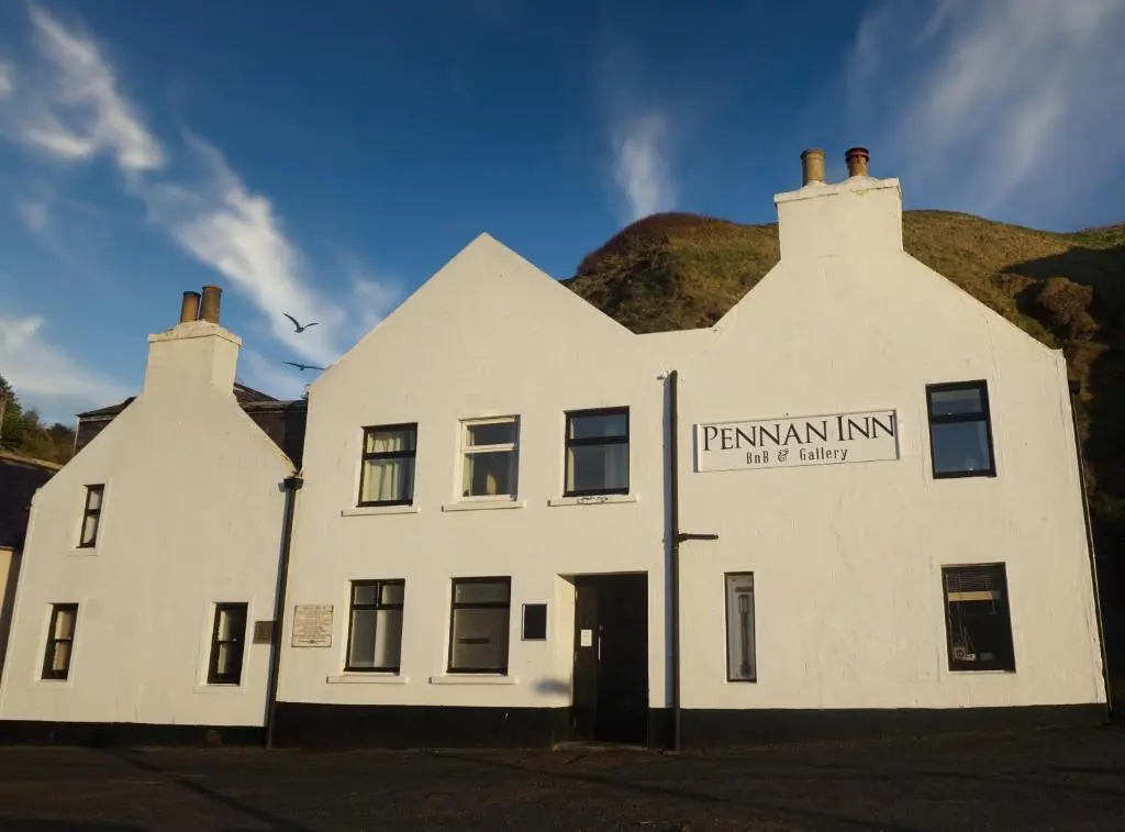 a white building with a hill in the background at The Pennan Inn in Pennan