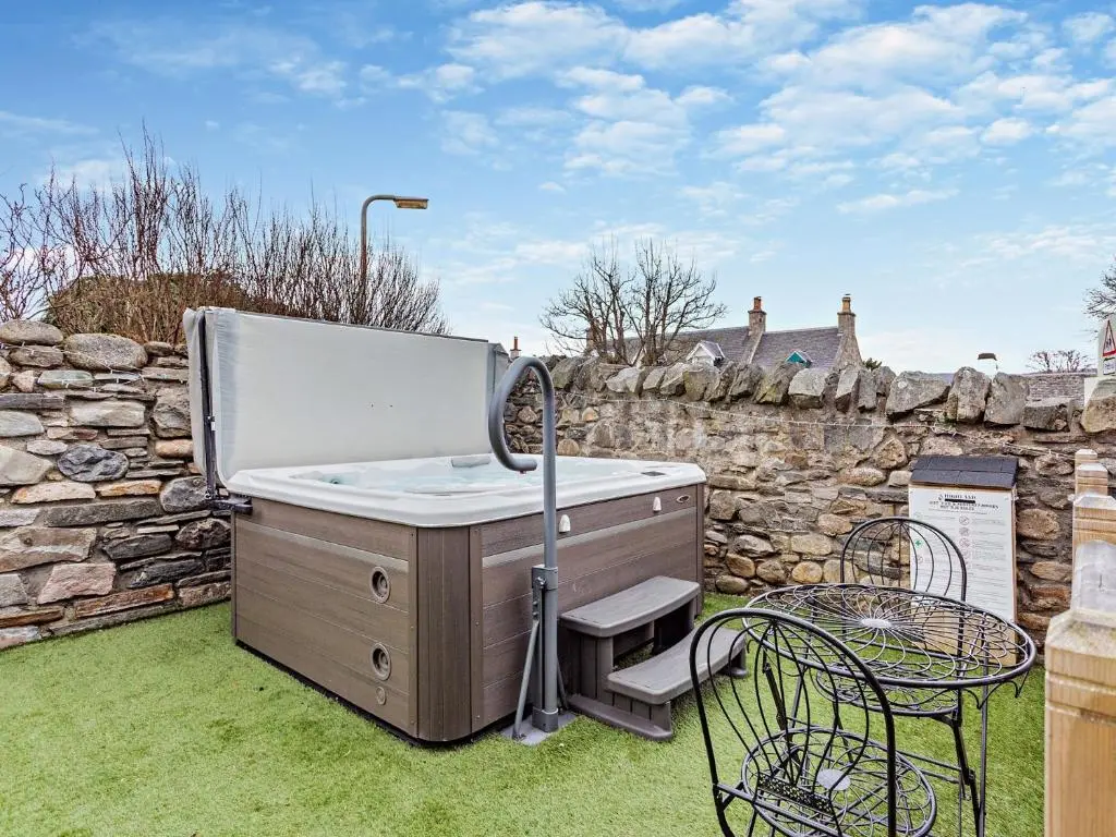 a hot tub in a yard with a stone wall at 3 Bed in Grantown-on-Spey 94514 in Grantown on Spey