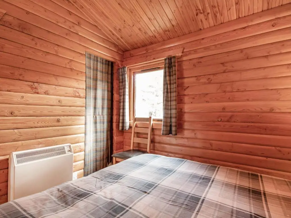 a bedroom with a bed in a wooden room at Lochside Log Cabin in Brora