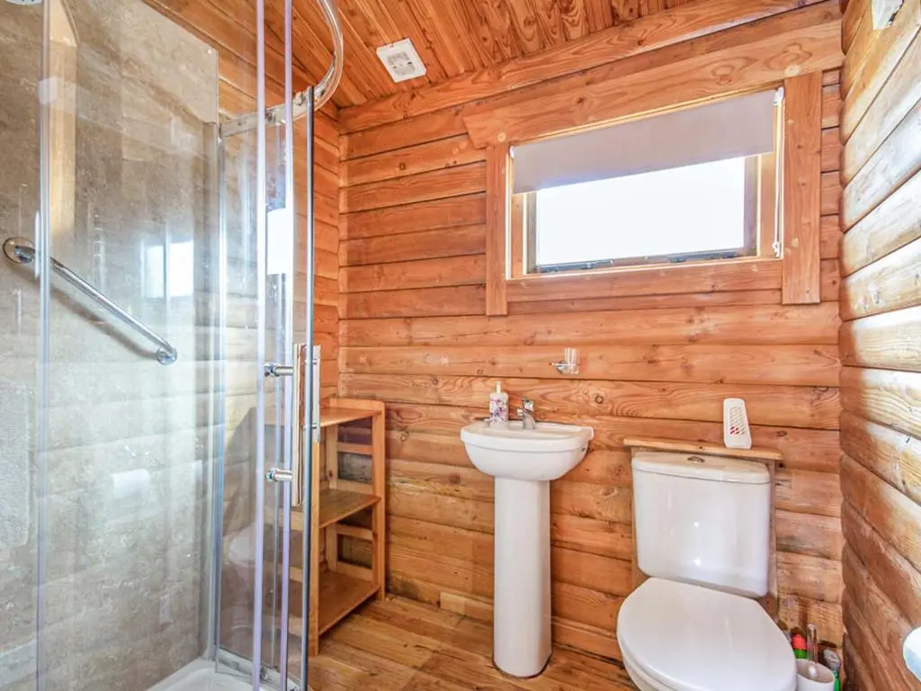 a bathroom with a toilet and a shower and a sink at Lochside Log Cabin in Brora