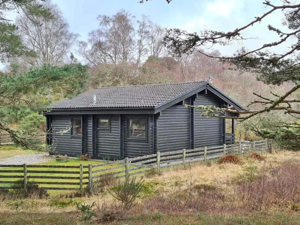 a black house with a fence in front of it at Lochside Log Cabin in Brora