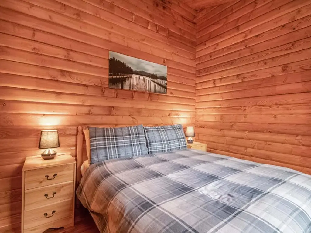 a bedroom with wooden walls and a bed and a night stand at Lochside Log Cabin in Brora