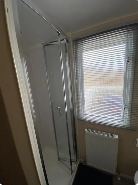 a bathroom with a glass shower with a window at Cozy\u2019s caravan hire in Lossiemouth