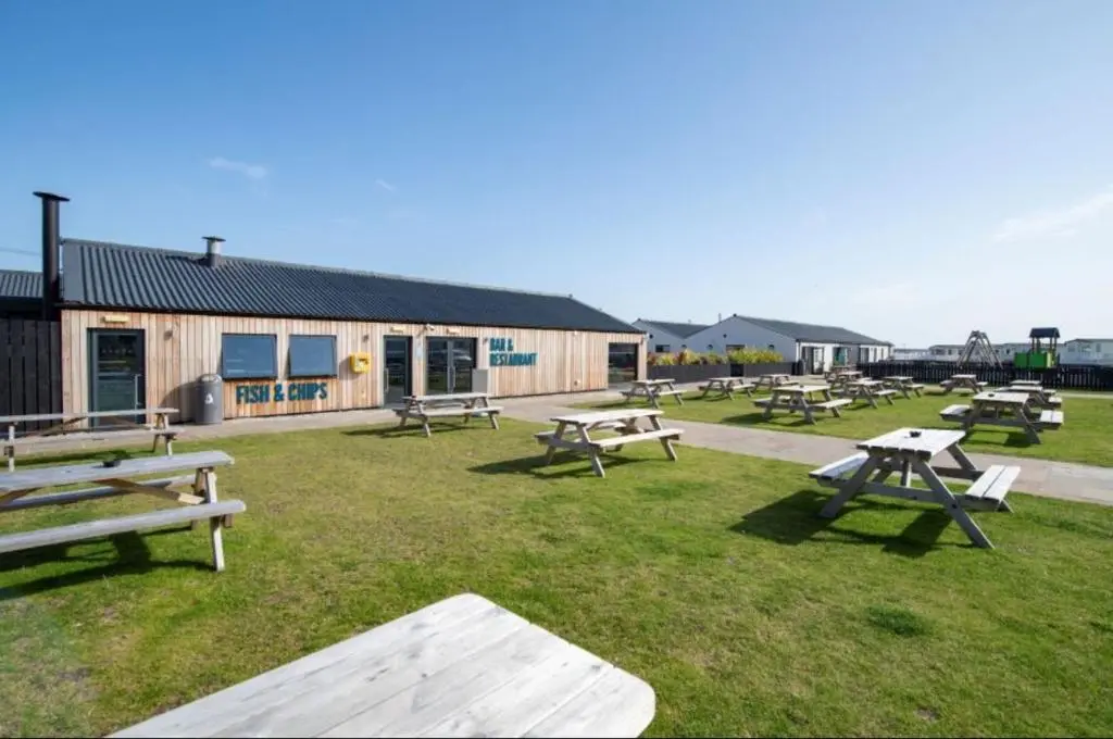 a group of picnic tables in the grass in front of a building at Cozy\u2019s caravan hire in Lossiemouth