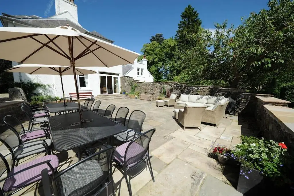 a patio with a table and chairs and an umbrella at Cray House - Large Country Home in Perthshire in Cray