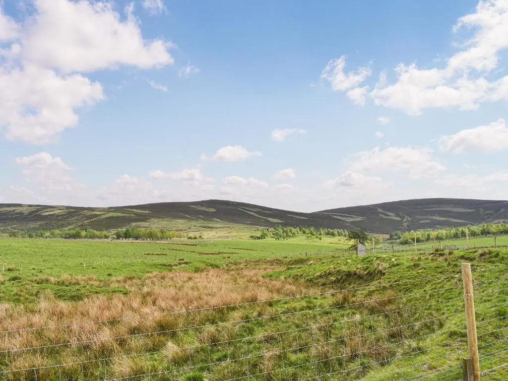 a fence in a field with hills in the background at Mid Bellandy in Ballindalloch