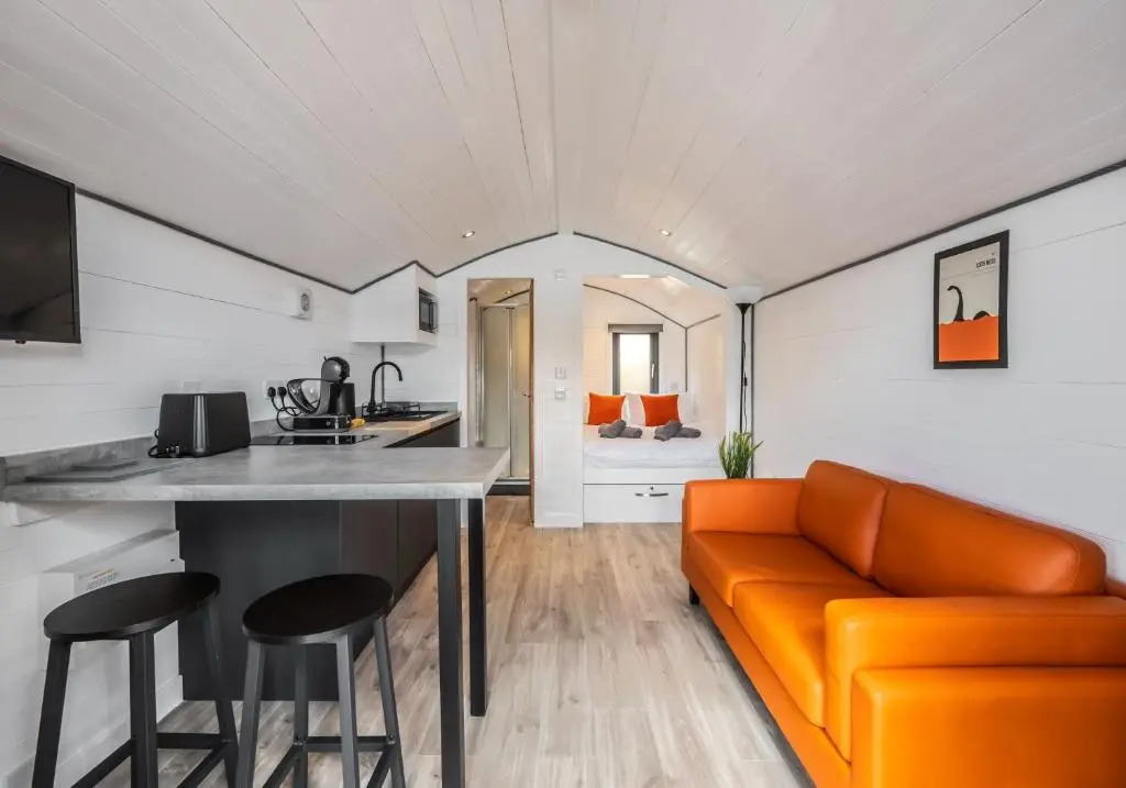 a living room with an orange couch and a kitchen at Alba Pod in Fort Augustus
