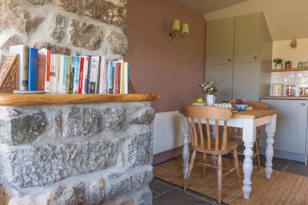 a room with a table with books on a stone wall at The Stable Bothy in Rogart