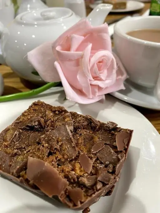 a piece of chocolate cake on a plate with a rose at Historical North Cottage in Old Deer in Old Deer