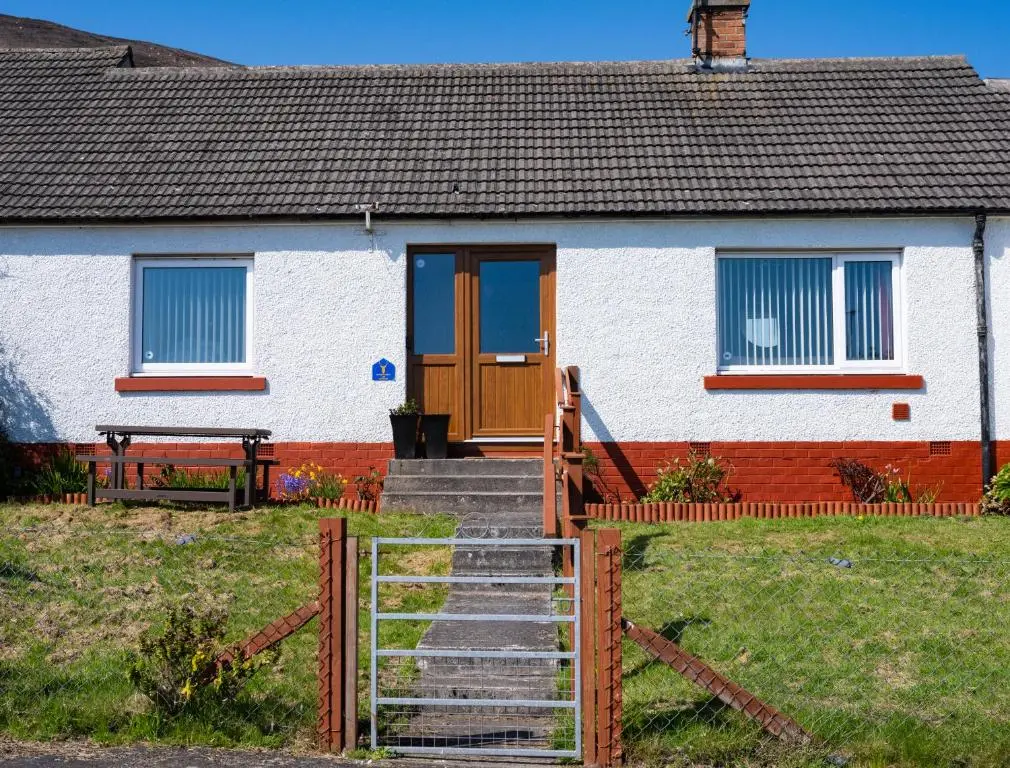 a house with a wooden door and stairs in front at North Coast Cottage - Coastal Highland Retreat with Sea Views in Portgower
