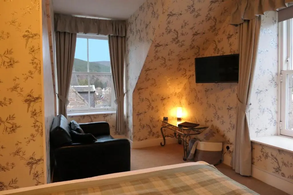 a bedroom with a bed and a chair and a tv at The Gordon Guest House in Ballater